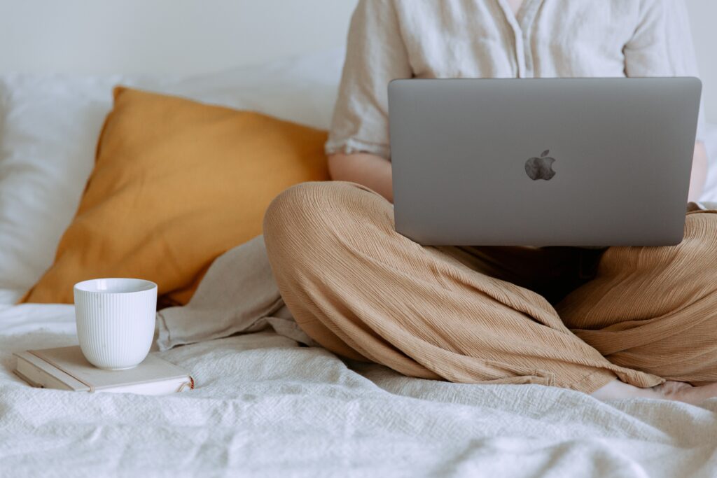girls sitting in bed with laptop on her lap and a cup of coffee