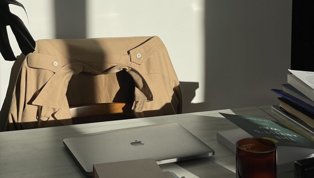 laptop on desk with books and candle with jacket on the chair